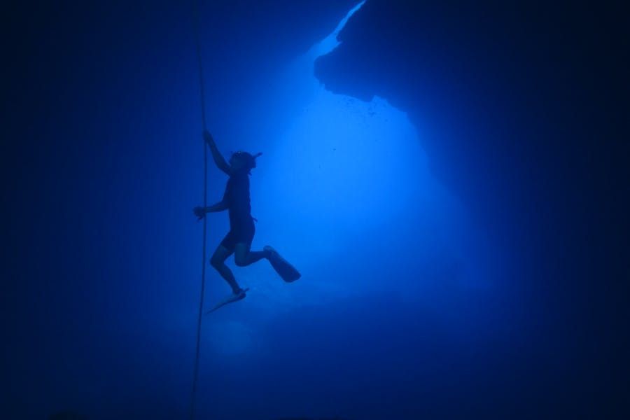 Freediver ascending through blue underwater cave