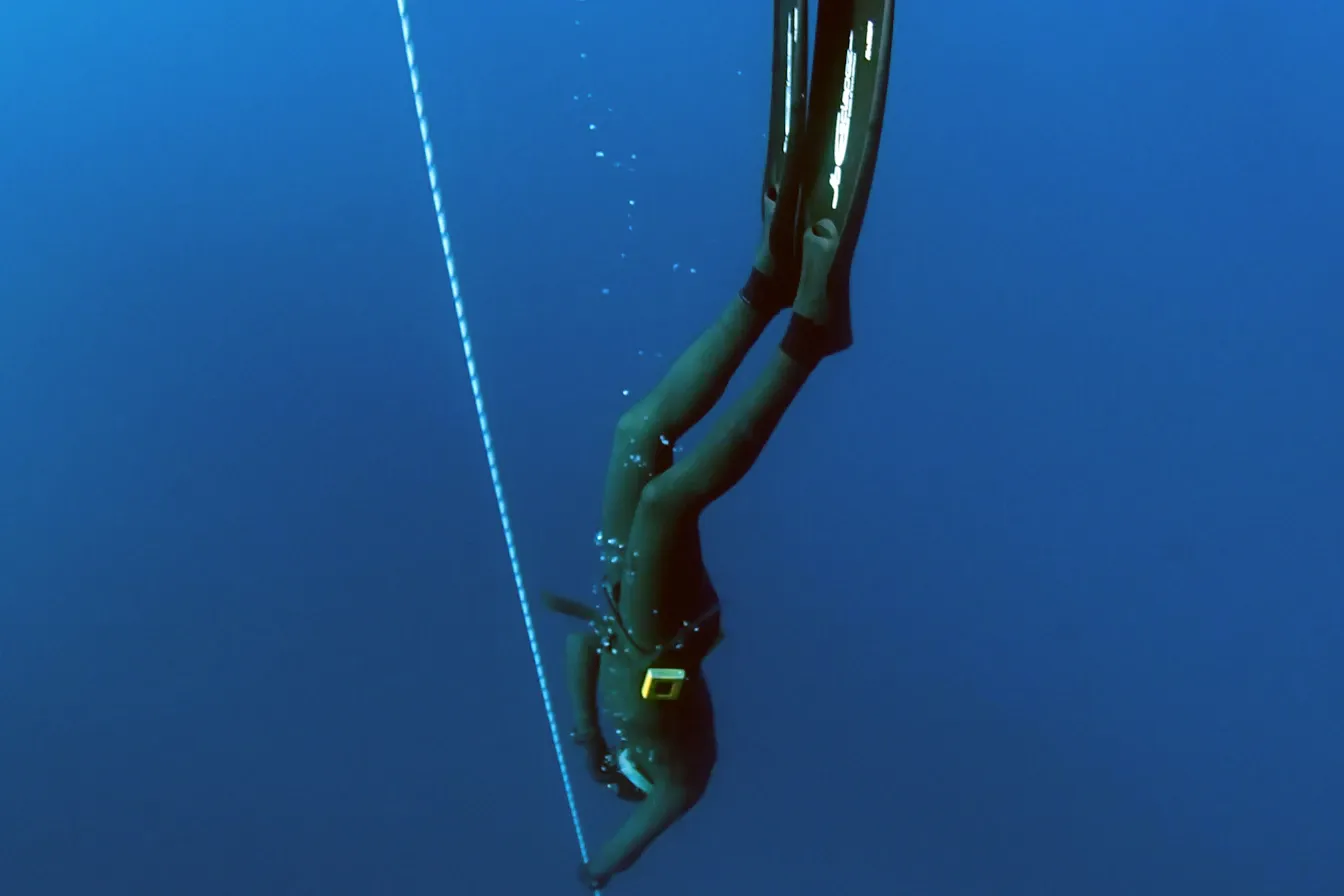 Freediver descending headfirst along a dive line into the deep blue