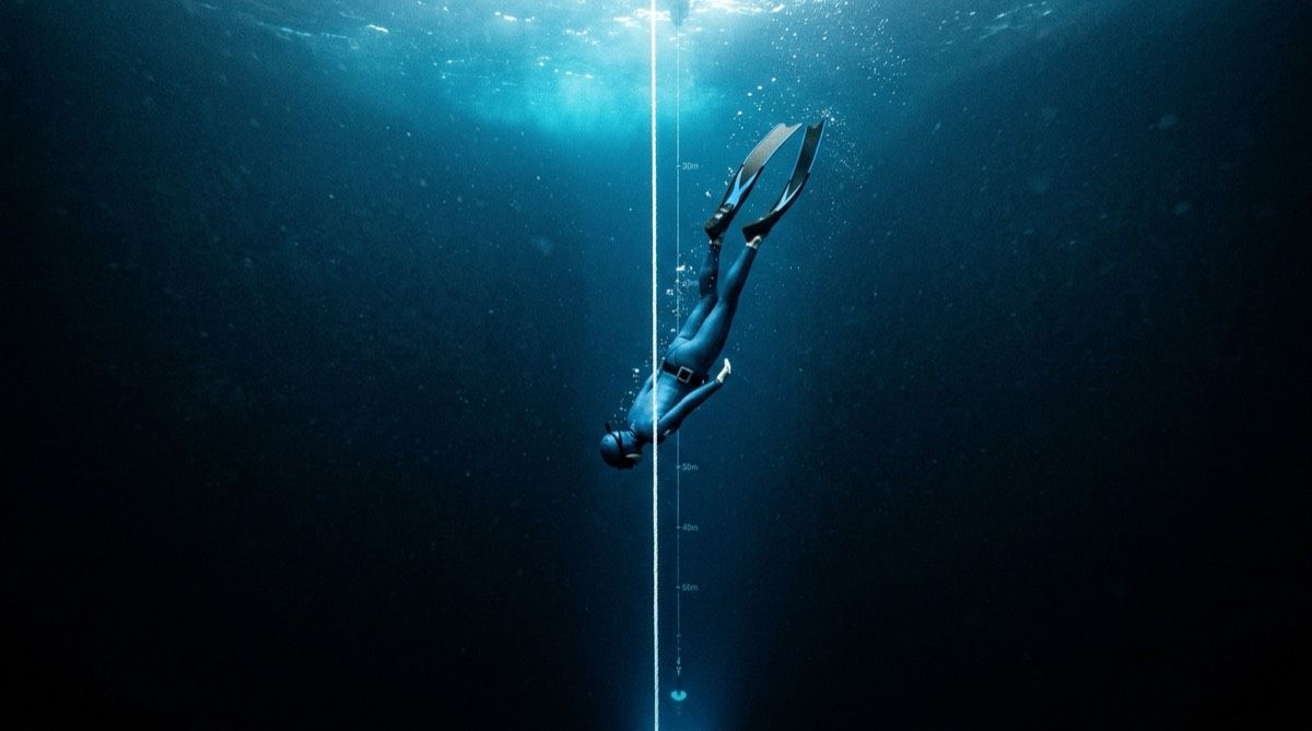 Freediver descending along a dive line into deep blue water